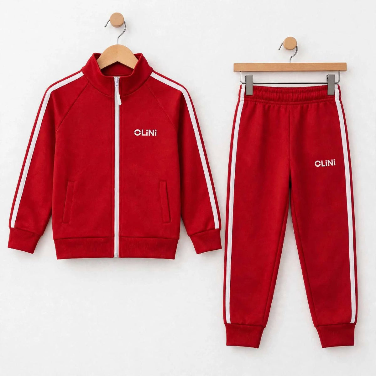 A two-piece kids' tracksuit set consisting of a red zip-up jacket and matching sweatpants, both with white side stripes and the brand name 'OLINI' printed in white on the chest, displayed on wooden hangers against a white wall.
