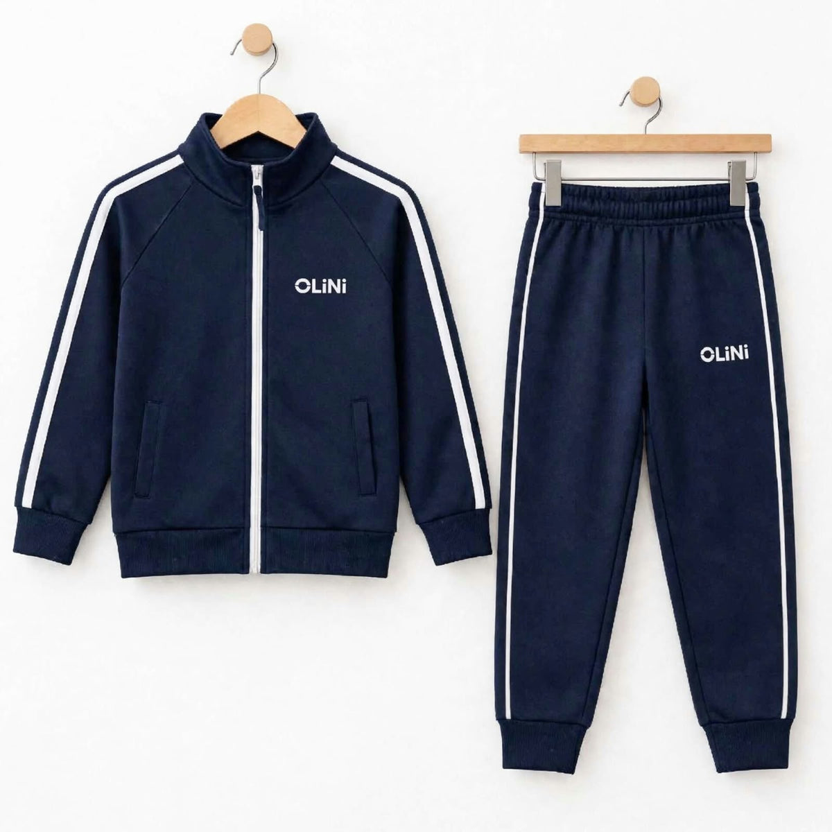 A two-piece kids' tracksuit set in navy blue, featuring a zip-up jacket with white side stripes and matching jogger pants, both hanging on wooden hangers against a white background.