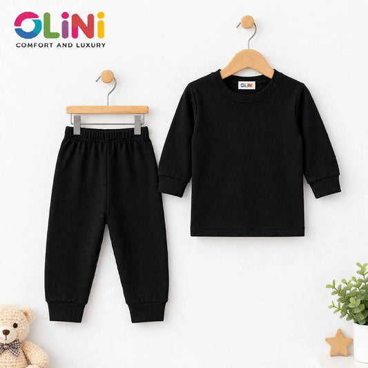 A two-piece children's outfit set by OLiNi, featuring a black long-sleeve top on a wooden hanger and matching black pants on a metal hanger, displayed against a clean white background with a small teddy bear and plant props.